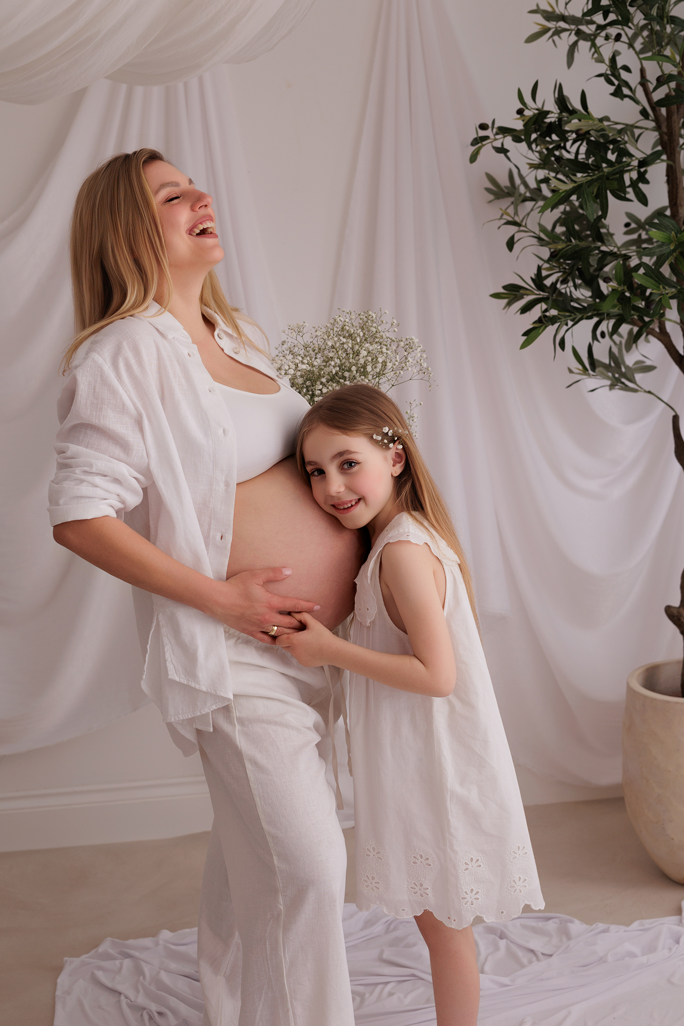 Natural maternity photo of pregnant mother and her young daughter hugging baby bump in soft light